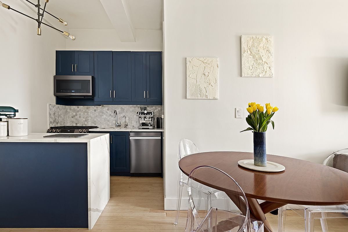 Open kitchen with navy cabinetry, white quartz island, stainless appliances, marble hex tile backsplash and a tulip-topped dining table in the foreground