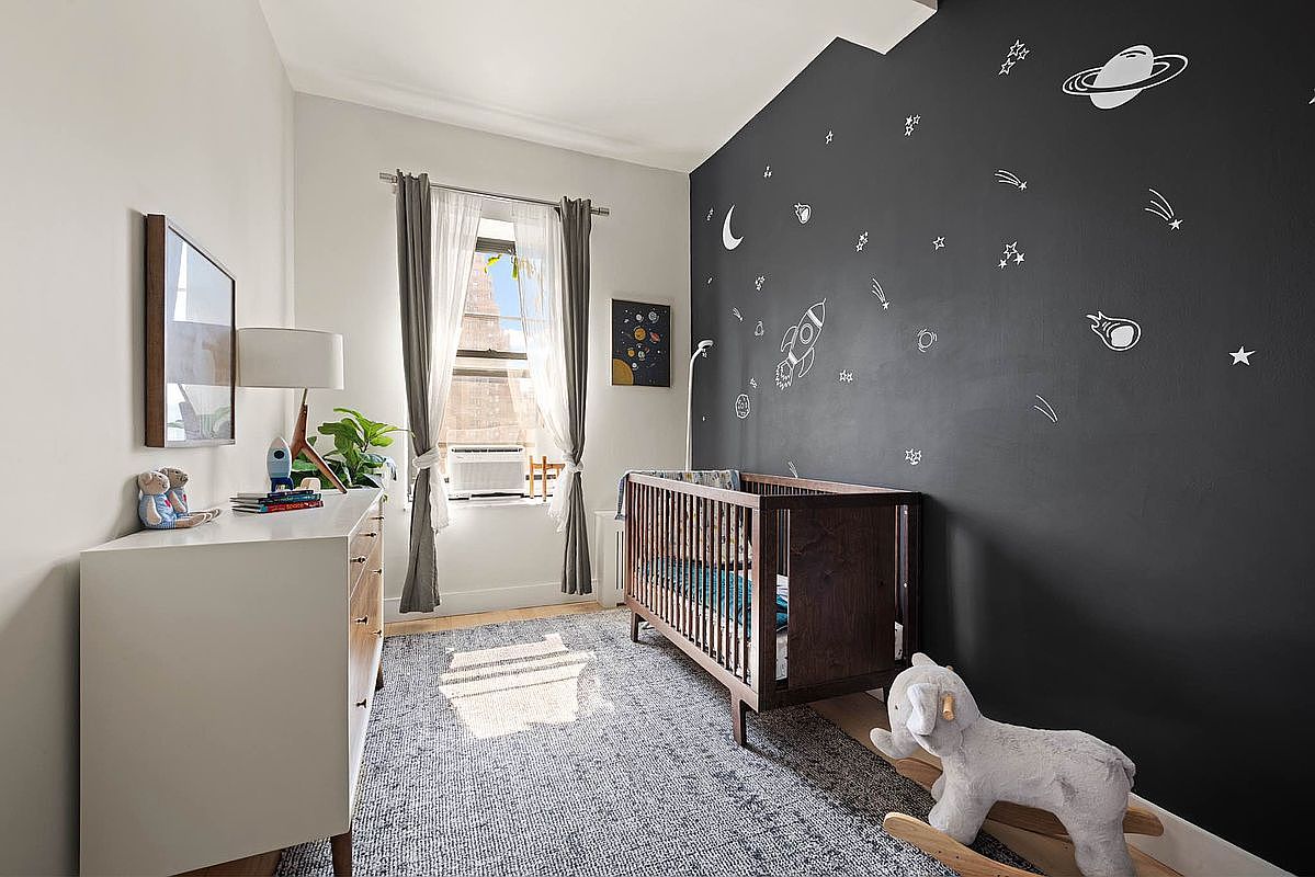 Second bedroom currently used as a nursery with a chalkboard accent wall, wooden crib, white dresser and east window